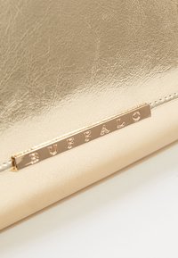 Złocista kopertówka ze sztucznej skóry o gładkiej fakturze, zdobiona metalową plakietką z napisem "BUFFALO" oraz cienkim paskiem.