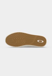 Semelle d'une basket décontractée avec une semelle en caoutchouc marron présentant des motifs ondulés et linéaires et un logo ovale blanc près du talon.