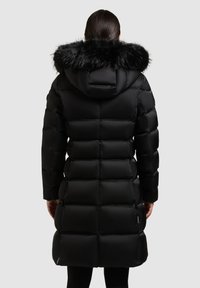 Must puffer-jakk kinnitatava karusnahast kapuutsiga, tikitud muster, pikk siluett ja tõmblukuga taskud. Sile, läikiv tekstuur.