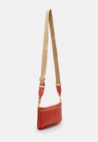 Bolso cruzado de cuero rojo con un acabado texturizado, que presenta un zipper dorado y una correa de hombro ajustable color beige. Diseño compacto y elegante.
