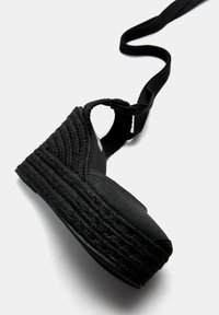 Svart espadrille kilklack sandal med en vävd juteplattform, tygöverdel och justerbar ankelsnodd. Slät textur med minimalistisk design.