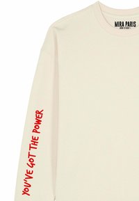 Felpa color crema con maniche lunghe. Presenta un testo rosso sulla manica sinistra con la scritta "YOU'VE GOT THE POWER." Nome del marchio visibile sul collo.