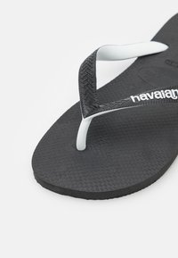Svart gummiflip-flop med en teksturert såle, hvit Y-formet stropp og merkevarelogo på stroppen. Designet for uformell bruk.
