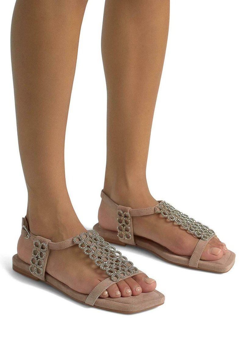 Płaskie sandały z koralikami z jasnoróżową, miękką górą tekstylną, z designem T-páska i płaską podeszwą. Styl odkryto-palczasty z dekoracyjnymi zdobieniami.