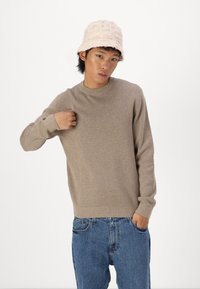 Pulover bej cu guler rotund și mâneci lungi, realizat dintr-un material moale. Asortat cu blugi din denim albastru deschis. Modelul poartă o pălărie texturată de tip bucket.