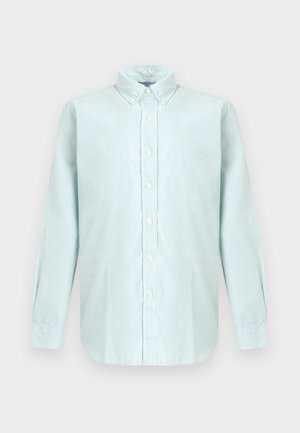 Chemise bleu clair à manches longues avec boutons, col boutonné, boutons blancs et ourlet arrondi sur fond neutre.