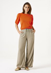Oranje kortetermijn top met puffmouwen, gecombineerd met lichtbeige brede broek met elastische tailleband en zijzakken.