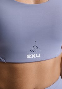 Svetlofialová športová podprsenka z textúrovaného, pružného materiálu. Obsahuje logo na spodnej časti a bodkovaný vzor nad ním.