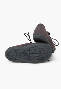 Zapatos de ante gris oscuro con puntera redondeada, suela de goma plana y diseño de cordones. Patrón de suela texturizada notable con caras sonrientes.