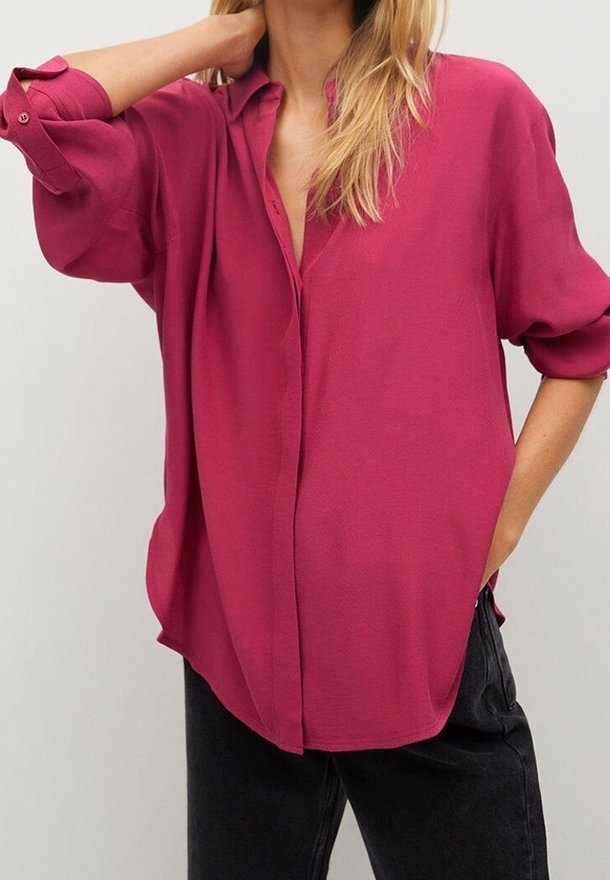 Fuchsia Button-up Hemd mit lockerem Schnitt, hochgekrempelten Ärmeln und seitlichen Schlitzen, kombiniert mit dunklen Denim-Hosen. Glatte Textur, klassisches Kragen Design.