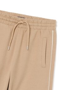 Beige Fleece-Jogginghose mit einem Kordelzugbund, seitlichen Taschen und weißen Paspeln an den Seiten. Weicher Stoff, lässiges Design.