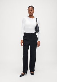 Black tailored trousers with a relaxed fit, worn with a fitted white long-sleeve top. Accessories include a small black shoulder bag and pointed heels.
