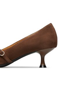 Pompe in suede marrone con punta arrotondata, tacco conico basso e cinturino decorativo con accentuazione in fibbia metallica. Texture liscia, design elegante.