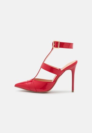 Chaussure à talon haut en cuir verni rouge à bout pointu, avec bride à la cheville, deux bandes horizontales et une fermeture à boucle dorée.