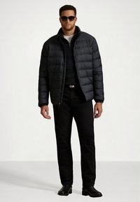 Crna jakna s vodoravnim šavovima, u kombinaciji s crnim džemperom i trapericama. Model nosi sunčane naočale i crne čizme.