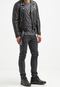 Svart läderbikerjacka med silverfärgade dragkedjor, grå texturerad t-shirt, svarta skinny jeans och svarta mönstrade sneakers.