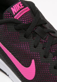 Černá sportovní bota s růžovými akcenty, která má síťovanou svrchní část, texturovaný povrch a výrazné růžové logo Nike swoosh.