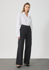 Fekete, magas derekú, széles szárú farmernadrág, amely egy sima, fehér, hosszú ujjú, lazán szabott inggel van párosítva.