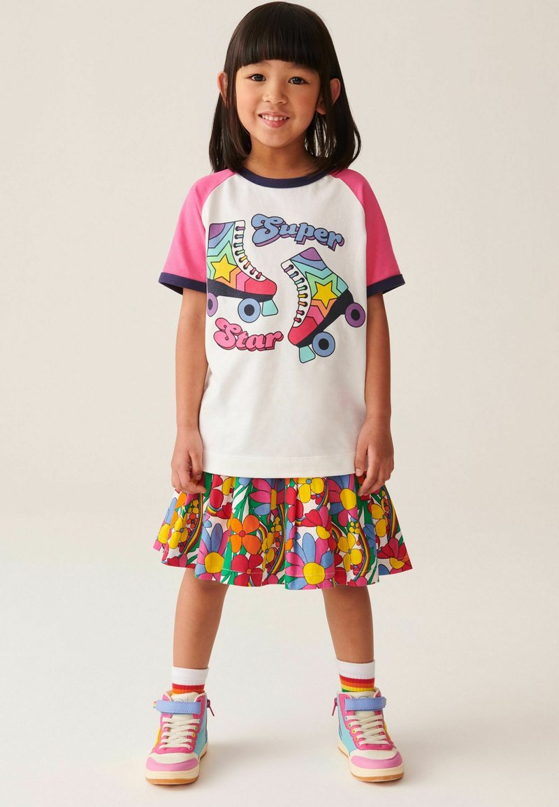 Hvid t-shirt med pink ærmer og grafik af rulleskøjter, parret med en farverig blomster-pleated nederdel og pastelfarvede sneakers.