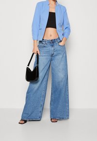 Lichtblauwe cropped blazer, zwarte cropped top, wijde denim jeans en een kleine zwarte handtas. De textuur is soepel; de denim heeft een vervaagde wassing.