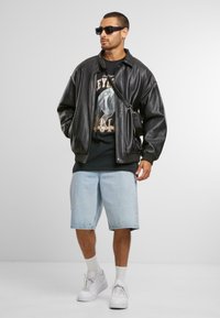 Must have musta nahktagi, graafiline must T-särk, helesinised teksase shorts, valged tennisetossud, valged sokid ja mustad prillid.