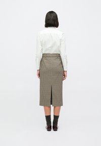 Καφέ midi φούστα με καρό μοτίβο, εφαρμοστή μέσ�η, πίσω σκίσιμο και υφή υφάσματος. Συνδυασμένη με λευκό πουκάμισο και σκουρόχρωμες κάλτσες.