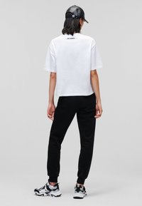 Bílý crop top, černé tepláky a černá baseballová čepice. Sportovní tenisky s bílými akcenty. Minimalistický design s detailem loga na topu.