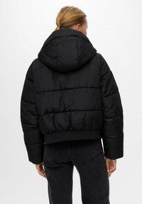 Giacca nera soffice con design cropped, grande cappuccio e sezioni trapuntate a vista. Presenta polsini e orlo elasticizzati per una vestibilità aderente.