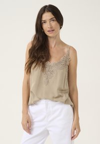 Débardeur beige avec des détails en dentelle délicate au niveau du col, des bretelles fines ajustables et une coupe décontractée, associé à un pantalon blanc.