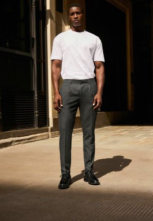 Weißes kurzärmliges T-Shirt kombiniert mit dunkelgrauen, maßgeschneiderten Hosen und schwarzen eleganten Schuhen, die eine klare, moderne Silhouette präsentieren.