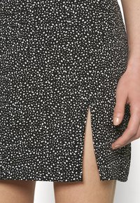 Černobílé skvrnité sukně se bočním rozparkem, který odhaluje stehno, vedle rozparku je ruka s jemně nalakovanými nehty.