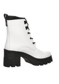 Botas blancas hasta el tobillo con una suela negra gruesa, que cuentan con un cierre de cordones en la parte delantera y una cinta en la parte trasera para ponerlas y quitarlas fácilmente.