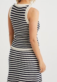 Ärmlös stickad klänning med marinblå och cremefärgade horisontella ränder, texturerad virkning och en figurnära silhuett.