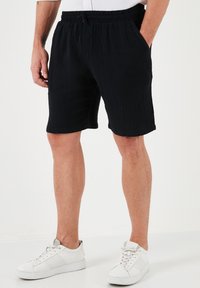 Zwarte shorts van gestructureerde stof met een elastische tailleband en trekkoord, voorzien van zijzakken en een relaxed fit. Draag met witte sneakers.