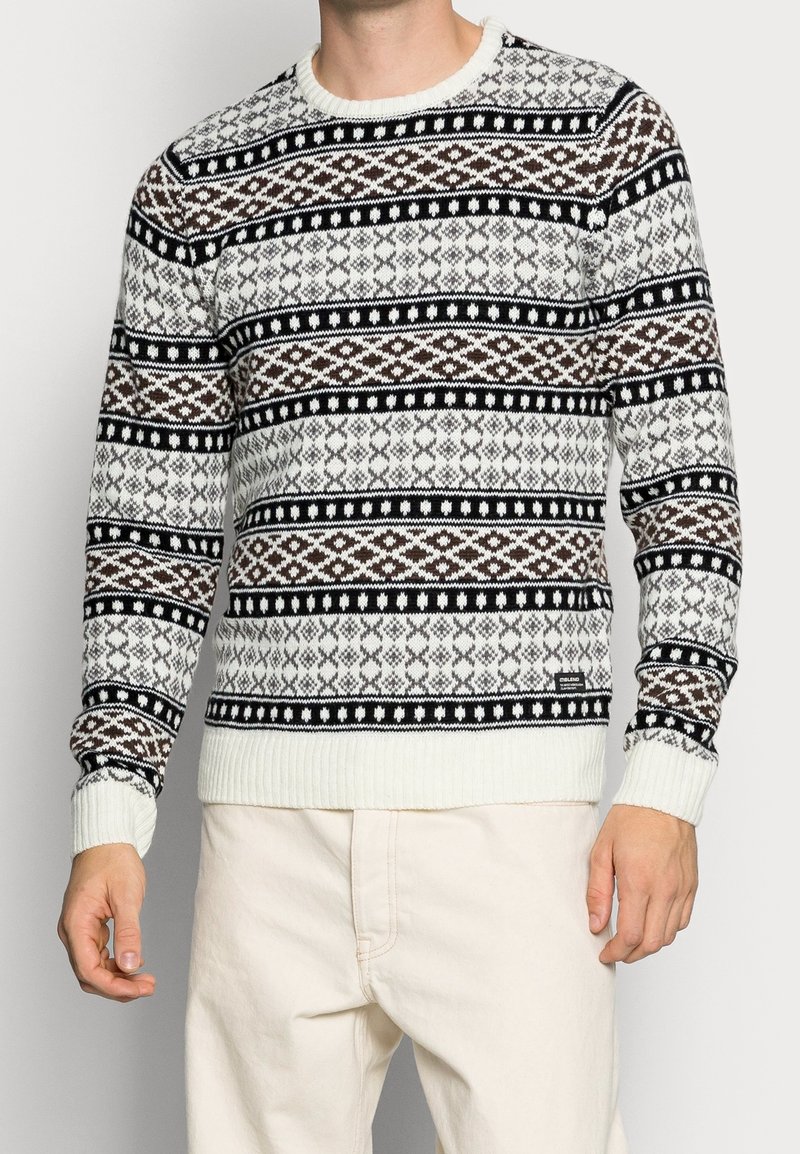 Neulottu neule, jossa on musta, ruskea ja valkoinen geometrinen kuvio; pyöreä kaula-aukko; neulotut resorireunukset hihansuissa ja helmassa; pehmeä tekstuuri.