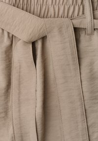 Pantalon en tissu coton beige avec une taille élastique et une large ceinture à nouer passant dans les passants de ceinture.