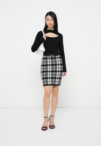 Μαύρο μακρυμάνικο τοπ με κοψίματα, συνδυασμένο με μία γκρι και μαύρη καρό φούστα μέχρι το γόνατο, με μαύρη ζώνη και λευκή τσάντα.