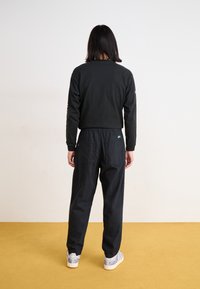 Black long-sleeve top with a crew neck, paired with black elastic-waist pants; both made of soft fabric and worn with patterned sneakers.