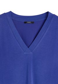 Bluzka z dekoltem w serek i krótkim rękawem, wykonana z gładkiego, fioletowego materiału. Posiada metkę na środku dekoltu z informacjami o marce.