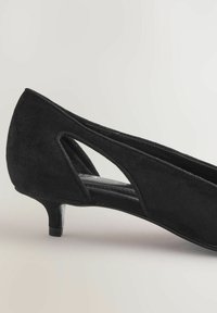 Crna antilop cipela s niskom tankom petom i bočnim izrezom na svijetloj pozadini.