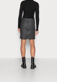 Gonna in pelle nera con un design aderente, due tasche posteriori e dettagli di cucitura in evidenza, abbinata a stivaletti neri alla caviglia.