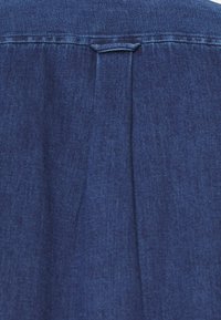 Tessuto di camicia in denim blu scuro con una superficie liscia, caratterizzato da un dettaglio a pieghe sul retro e cuciture a contrasto lungo le cuciture.
