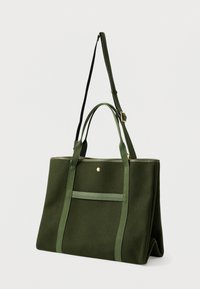 Zelená plátěná taška s dvojitými uchy a nastavitelným ramenním popruhem. Má přední kapsu a zlaté akcenty na zipu.