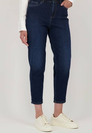 Donkerblauwe denim jeans met een fitted taille, taps toelopende pijpen en cropped lengte. Gestyleerd met een lichtgekleurde lange mouwen top en witte sneakers.