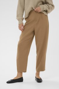 Pantalons larges couleur brun clair en tissu lisse, dotés d'une taille haute et de plis avant soigneusement pressés, accompagnés de ballerines noires.