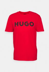 Camiseta de algodón roja con un gran logo negro "HUGO" en el frente, cuello redondo clásico, mangas cortas y un corte relajado.