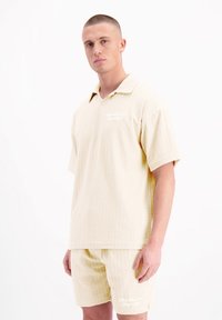 Korte mouw, geknoopte shirt en bijpassende shorts van een gestructureerde crèmekleurige stof met een golvend patroon en subtiele branding op het shirt.