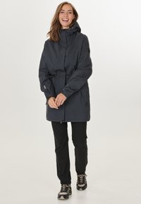 Mörkgrå vattentät jacka med åtstramad midja, justerbar huva, dragkedjefickor och elastiska ärmslut, tillsammans med svarta byxor och vandringskängor.