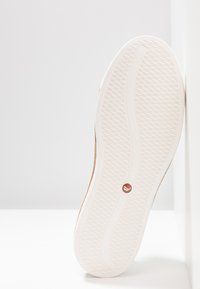 Sneakersohle mit einer strukturierten Gummi-Oberfläche, überwiegend weiß mit einer beige Seite und einem kleinen runden Akzent in der Mitte.