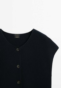 Laivastonsininen puuvillaneulottu neuletakki, jossa on resorikuvio, lyhyet hihat ja viisi suurta mustaa nappia edessä.